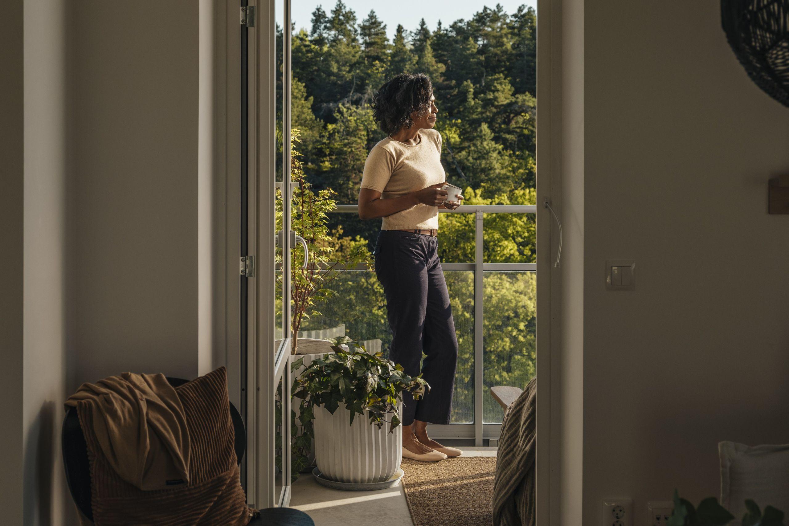 Kvinna står på en balkong och tittar ut över skogen.