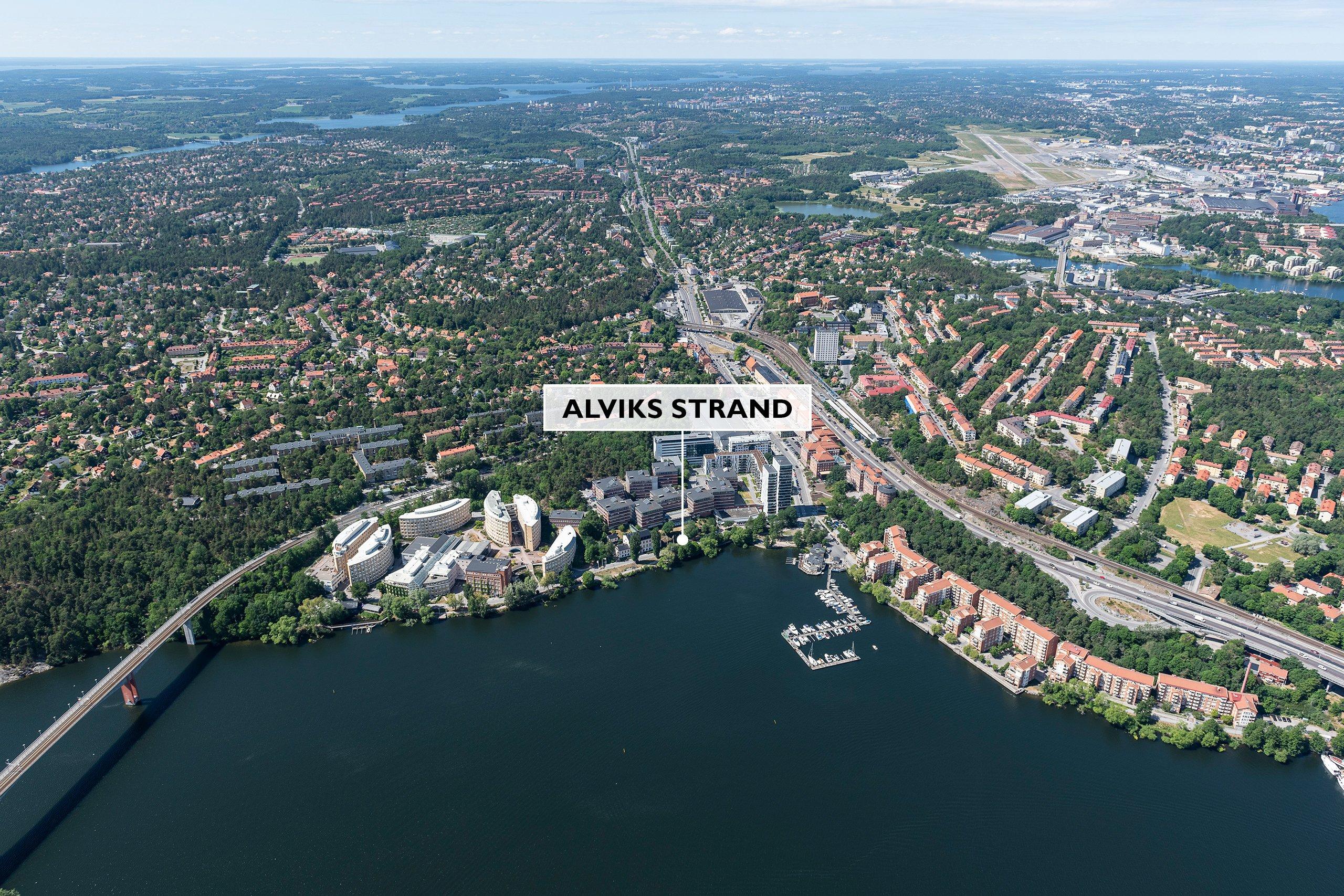 Vy från ovan över Alvik med blått vatten och stora grönområden, en textplatta visar var kvarteret Alviks strand kommer att byggas.