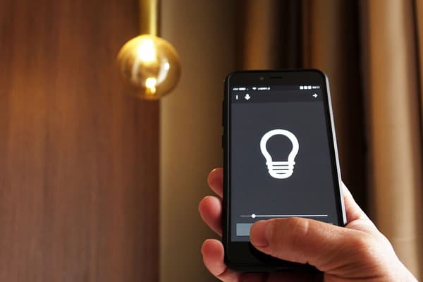 Hand håller en mobiltelefon med en app som kan styra smarta funktioner i ett nytt hem.
