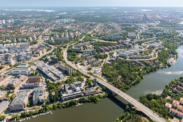 Solig vy över stadsbebyggelse med vägar, broar och vatten.