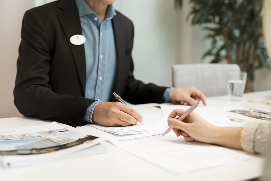 Person som sitter mitt emot en mäklare och skriver under ett kontrakt.
